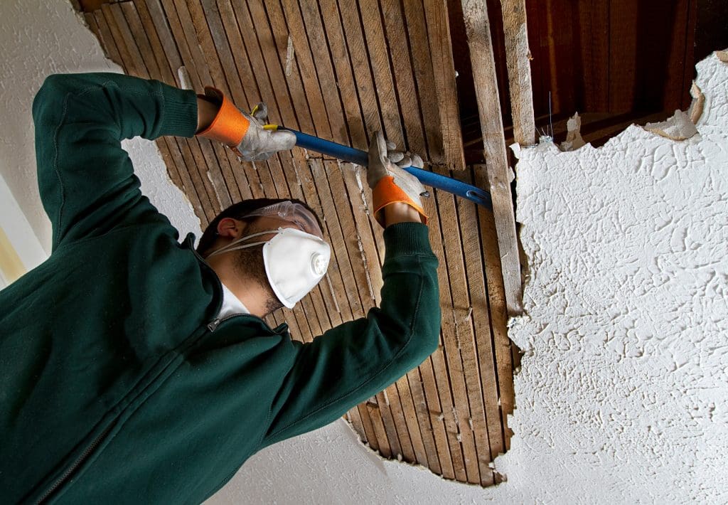a man pulling down plaster ceiling lathe with a crowbar