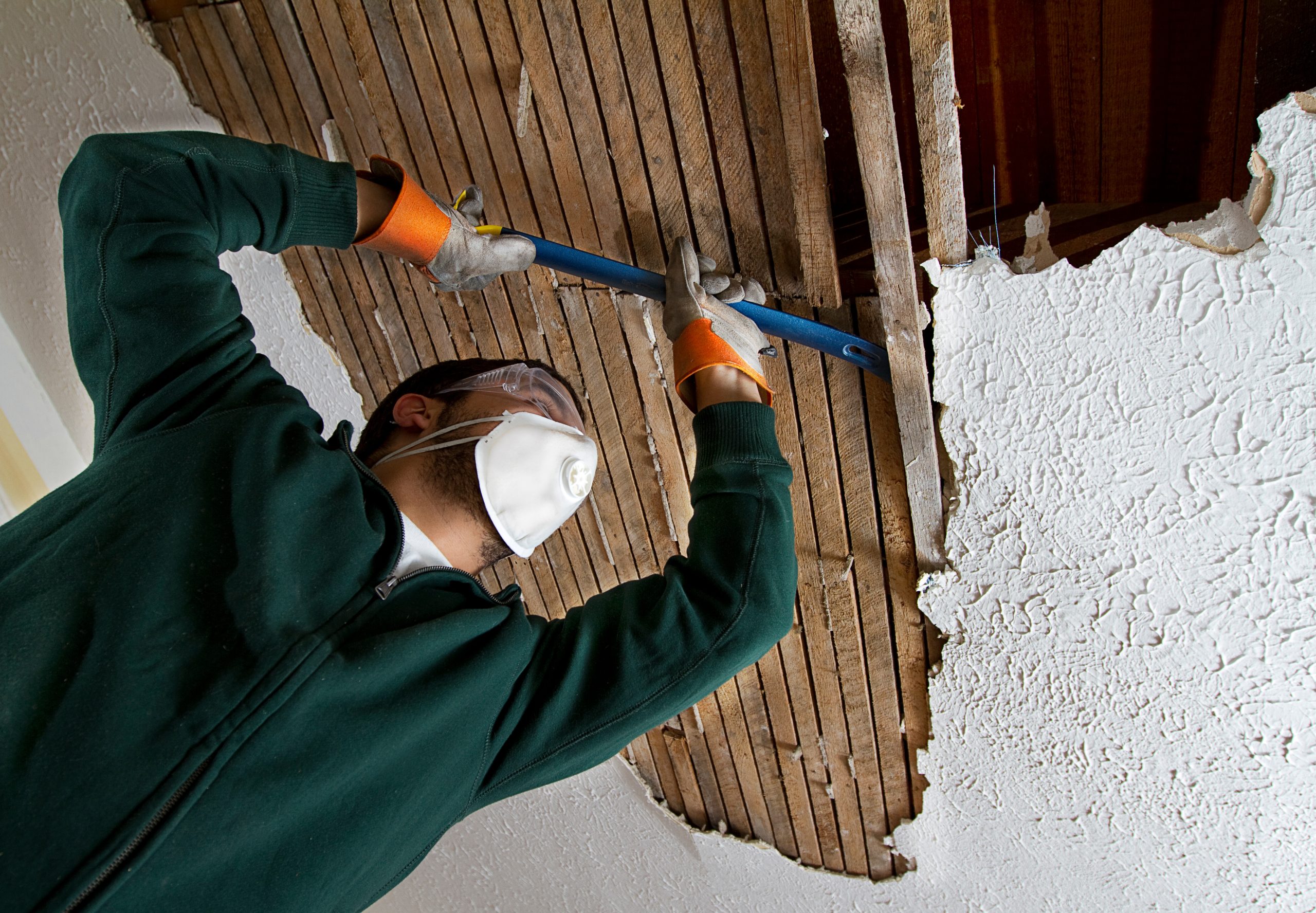 a man pulling down plaster ceiling lathe with a crowbar